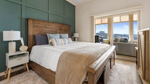 A bedroom with a large bed, wooden headboard, and a view of a cityscape through a large window.