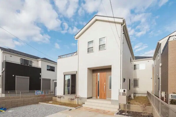 A modern two-story residential building with a flat roof, large windows, and a wooden front door.