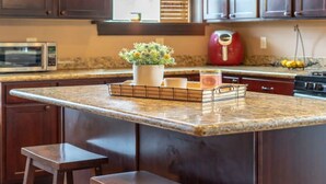 A kitchen with a granite countertop, dark wooden cabinets, a microwave, a red kettle, and a small potted plant. - Remodeled historic family home w/ full kitchen & garage parking (St. Louis)