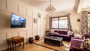 Ein Wohnzimmer mit einem großen Flachbildfernseher, einer violetten Sofagarnitur, einem Holztisch und einer Chandelüster.