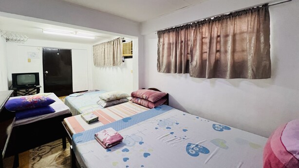 A small, well-lit room with two beds, a desk, and a television. - King Henrys Transient House (Bantay)