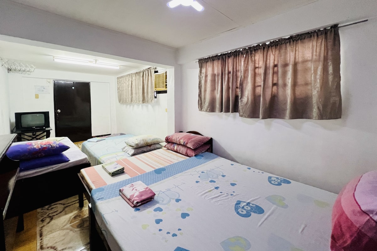 Una habitación pequeña y luminosa con dos camas, un escritorio y un televisor.