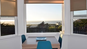 A dining area with a table and chairs, a view of the ocean, and a balcony with a railing. - Stunning ocean views close to beach and SF (Pacifica)