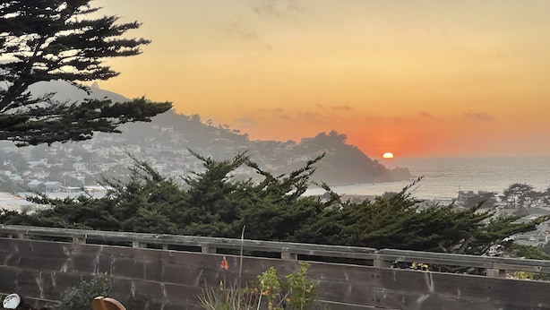 A wooden deck with a chair, overlooking a coastal cityscape during sunset. - Stunning ocean views close to beach and SF (Pacifica)