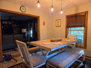 A dining area with a wooden table, benches, pendant lights, and a view of the outdoors through a window. - The Linville Community, a restful retreat watch the changing colors.  (Newland)
