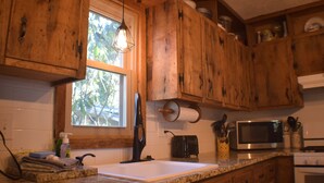 A kitchen with wooden cabinets, a granite countertop, a sink, a microwave, and a window with natural light. - The Linville Community, a restful retreat w/ convenient access to the mountains (Newland)