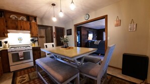 A kitchen with wooden cabinets, a stove, and a dining table with chairs. There is a clock on the wall and a small plant on the table. - The Linville Community, a restful retreat w/ convenient access to the mountains (Newland)