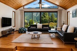 A spacious living room with a large TV, a black sofa, a coffee table, and a view of mountains through large windows. - Sublime Escape Central Location Parking & Fireplace (Queenstown)