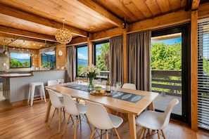 Un intérieur en bois comprenant une table à manger, des chaises, un coin cuisine et de grandes fenêtres avec des rideaux.