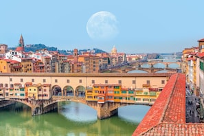 A historic cityscape with a prominent bridge, a river, and a large moon in the sky.