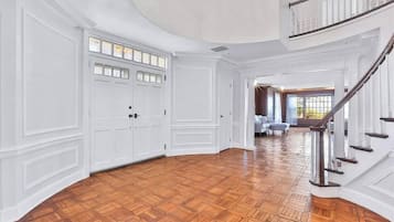 A spacious interior with a wooden parquet floor, white paneled walls, and a grand staircase.