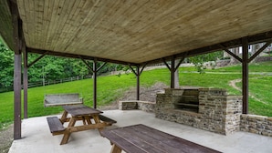 A covered picnic area with picnic tables and a stone fireplace.