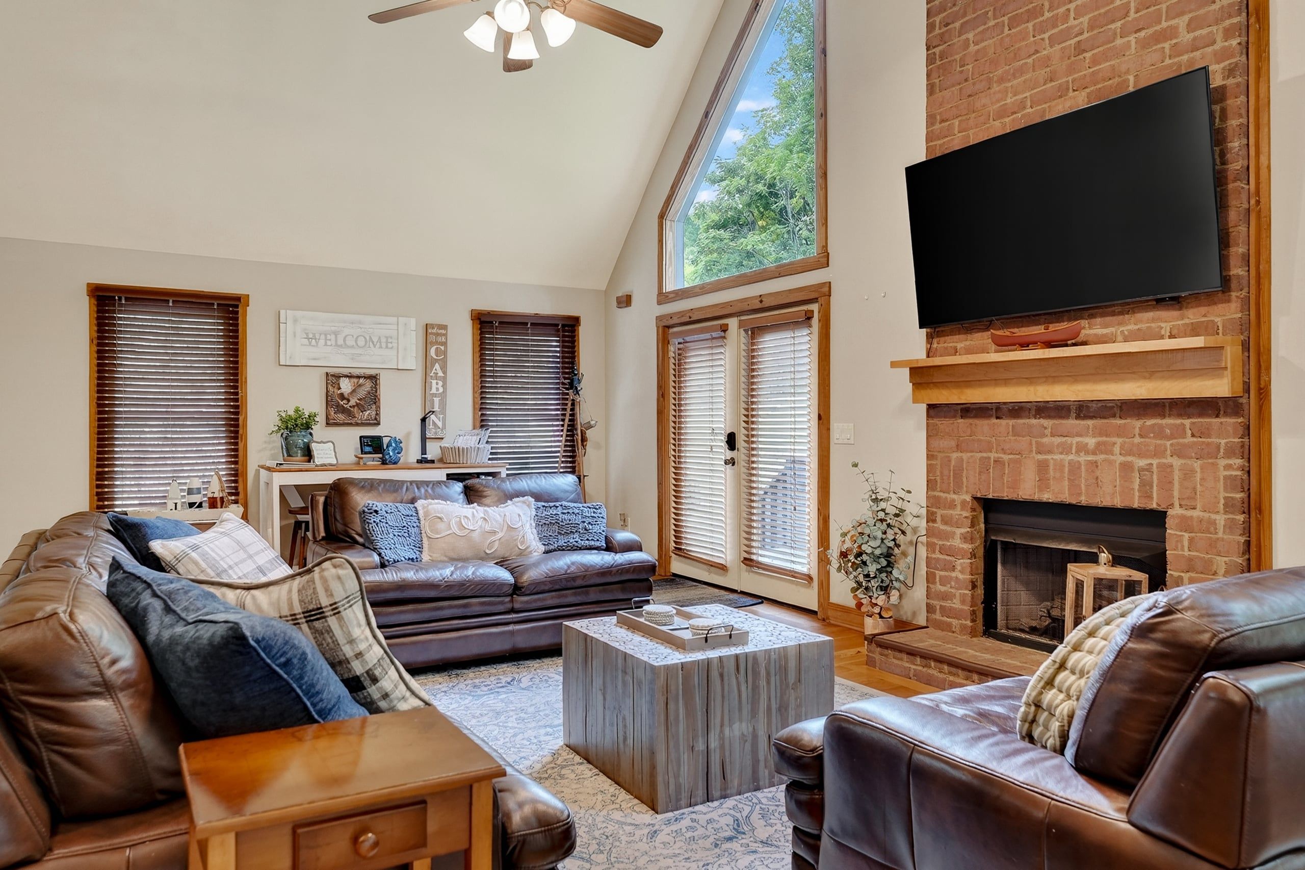 A spacious living room with a fireplace, leather sofas, a coffee table, and a flat-screen TV mounted above the fireplace.