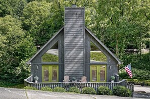 Eine Holzhütte mit Schornstein, zwei grünen Türen und einer Veranda mit Adirondack-Stühlen.