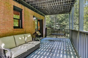 Eine überdachte Veranda mit einem Korbsessel und einem kleinen Tisch, einer Ziegelwand und einem Metallgeländer.