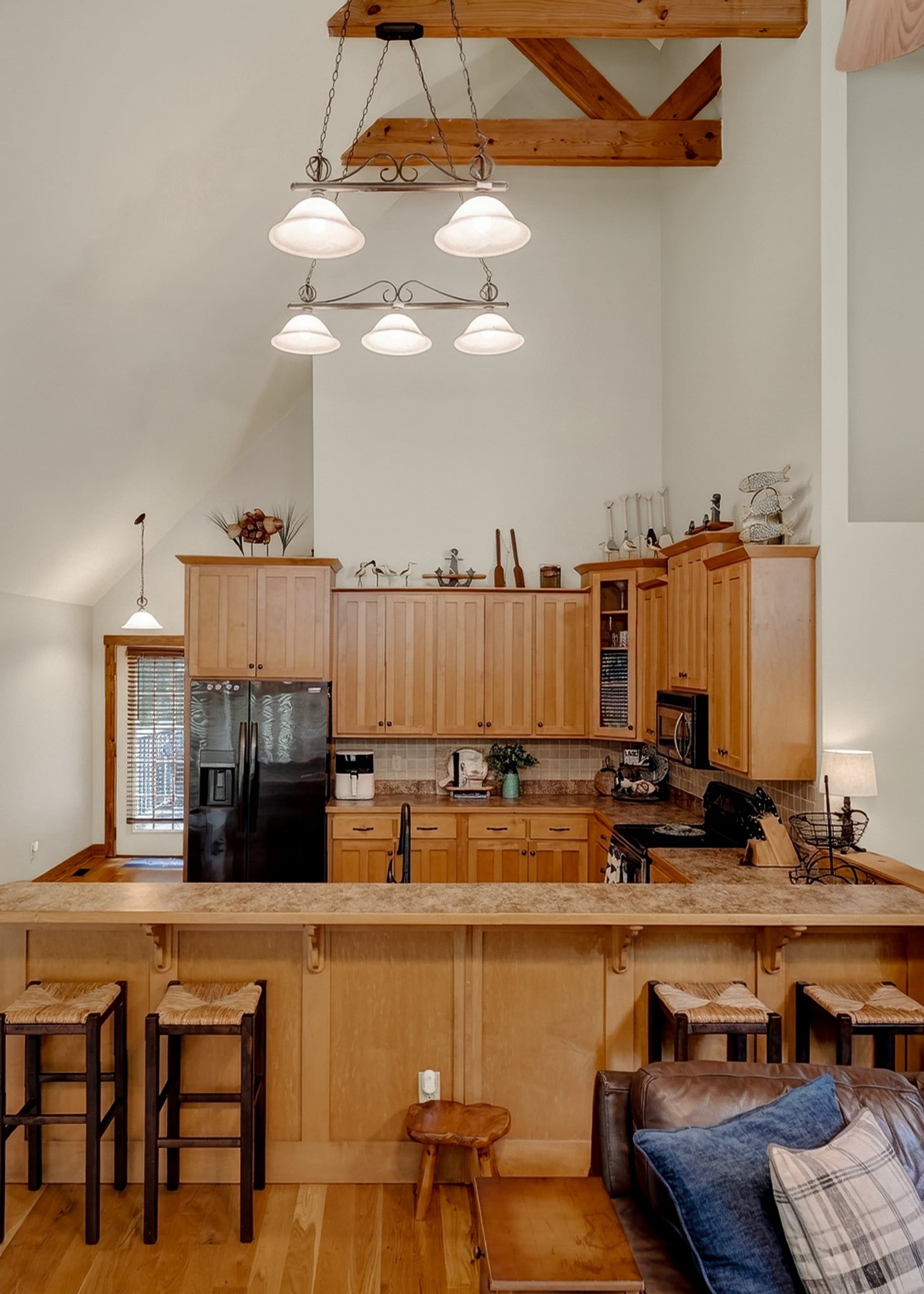 A kitchen with wooden cabinets, a black refrigerator, a wooden island with stools, and pendant lighting.