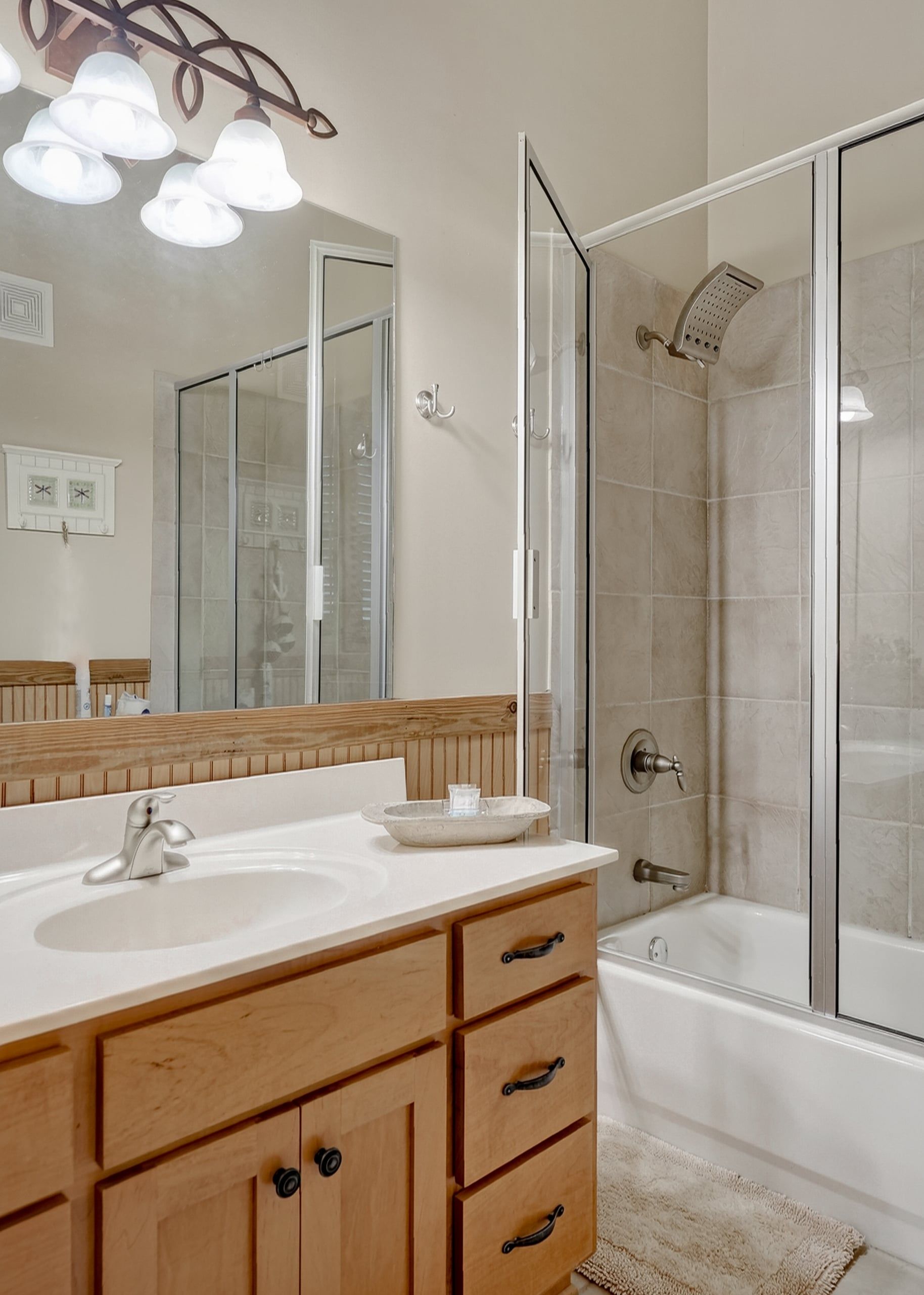 A bathroom with a white sink, wooden vanity, a mirror, and a glass-enclosed shower.