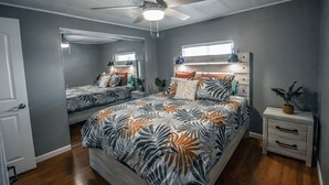 Un dormitorio con cama, mesita de noche, ventilador de techo y ventana.