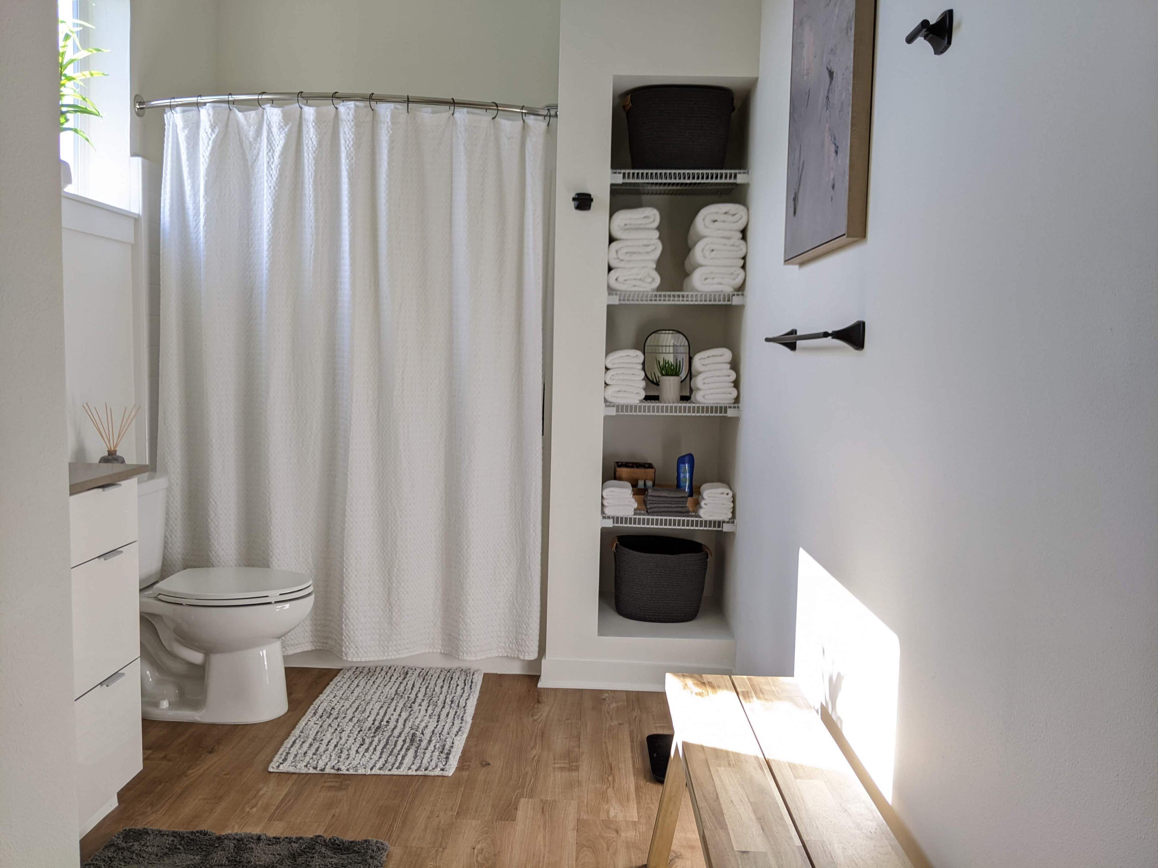 Et badeværelse med toilet, bruseforhæng, vask og hylder med håndklæder.