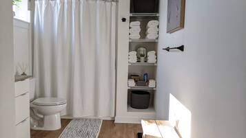 Et badeværelse med toilet, bruseforhæng, vask og hylder med håndklæder.