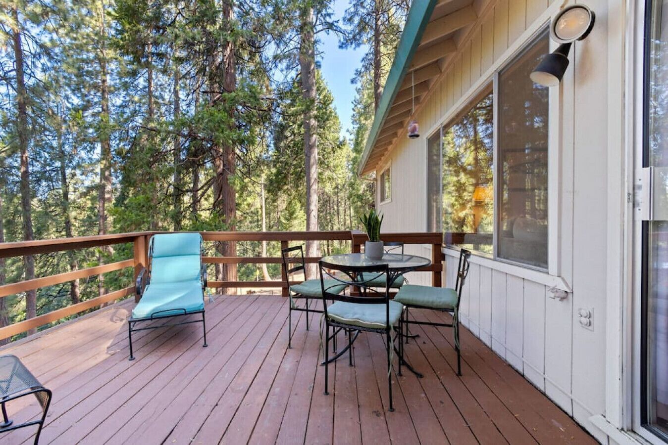 A wooden deck with outdoor furniture, surrounded by tall trees.