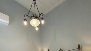 A neatly made bed with two pillows and a folded towel, a bedside table with a lamp, and a wall-mounted light fixture. - Two-story mansion in the historical center Ermoupolis. Close to (Ermoupoli)
