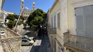 A narrow cobblestone street with buildings on either side, a church with a bell tower, and a clear blue sky. - Two-story mansion in the historical center Ermoupolis. Close to (Ermoupoli)