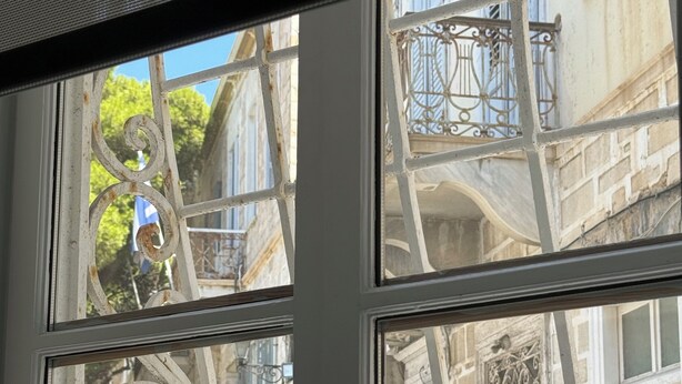 A window with ornate metal grilles and a view of old buildings. - Two-story mansion in the historical center Ermoupolis. Close to (Ermoupoli)