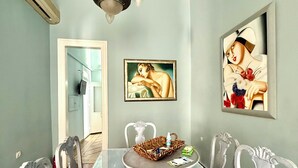 A dining room with a glass table, white chairs, a chandelier, and two framed artworks on the walls. - Two-story mansion in the historical center Ermoupolis. Close to (Ermoupoli)