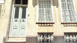 A building with a white door, multiple windows with metal grilles, and decorative iron railings on balconies. - Two-story mansion in the historical center Ermoupolis. Close to (Ermoupoli)