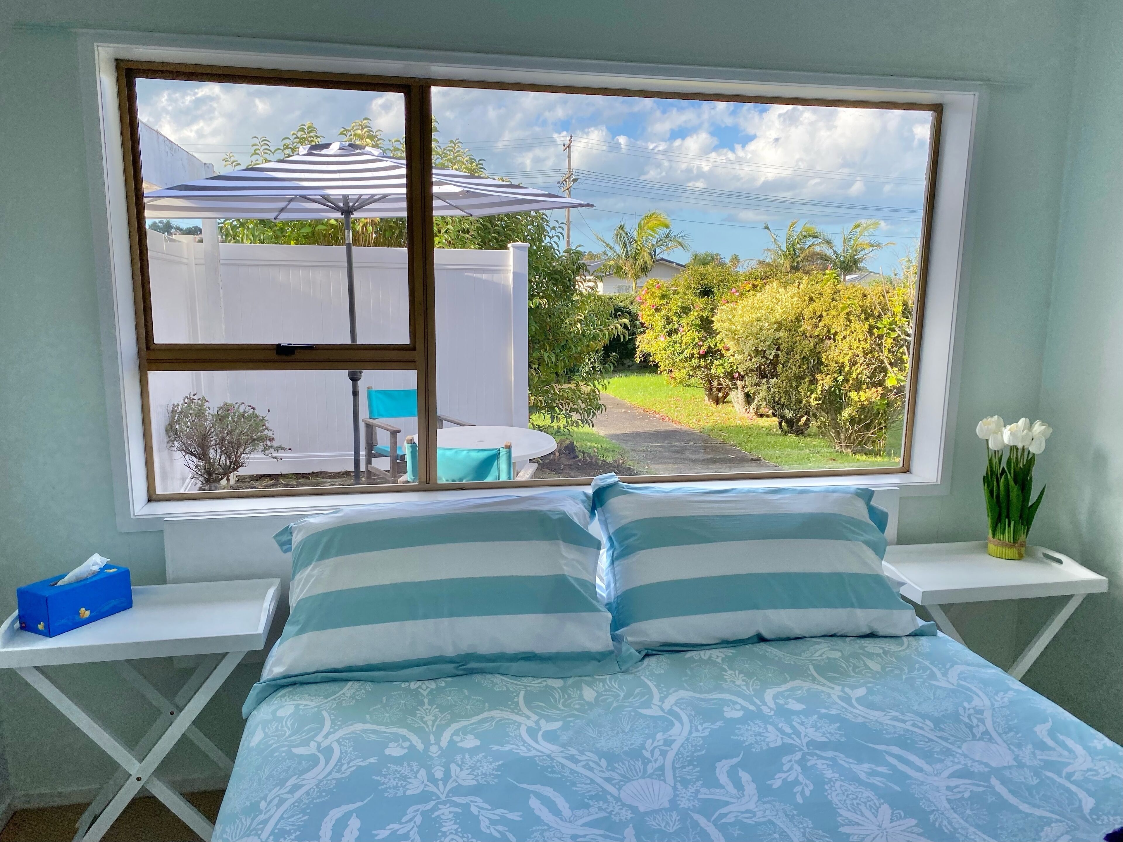 A bedroom with a bed, two nightstands, a window with a view of a backyard, and a vase with flowers.