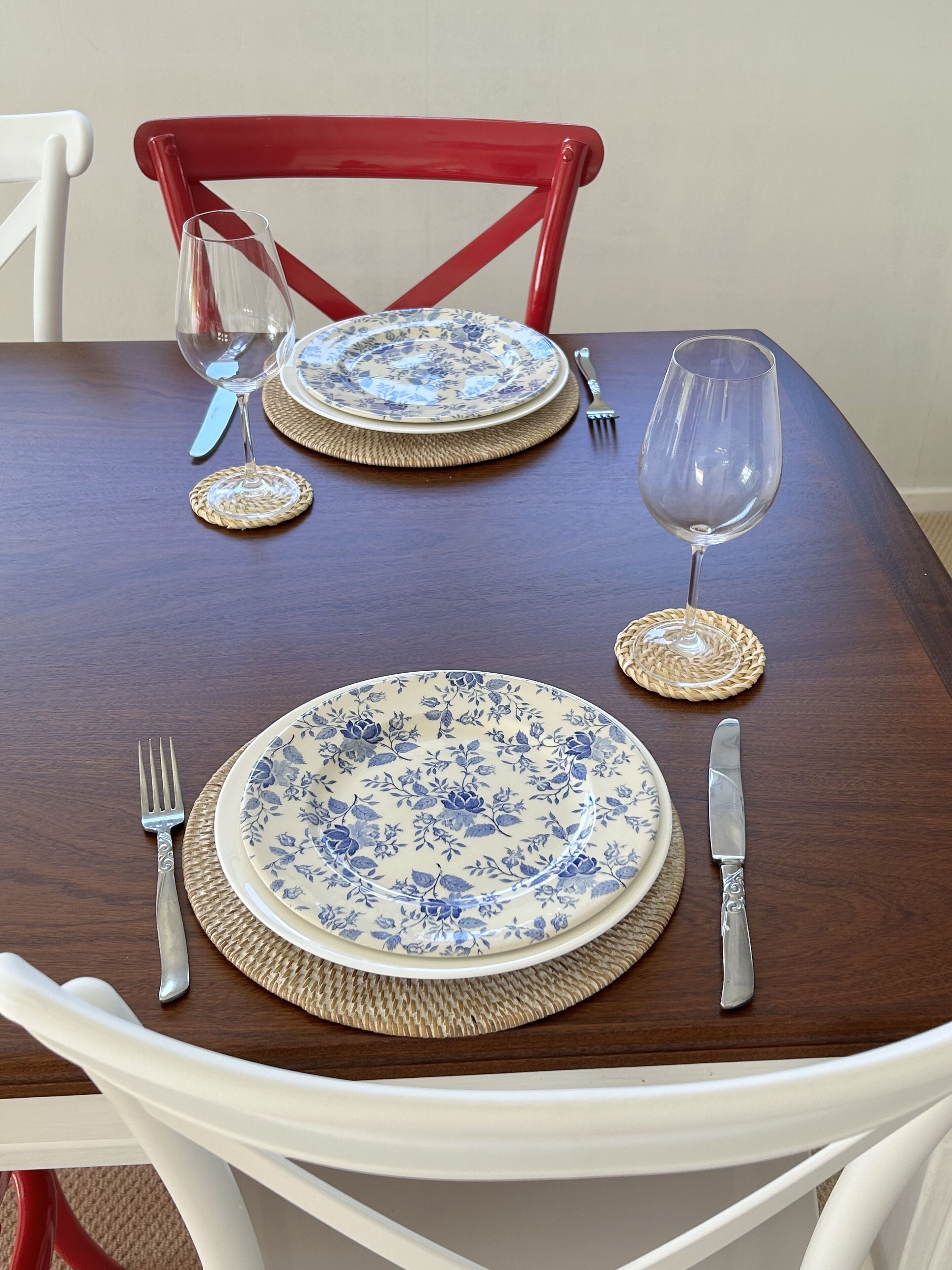 A dining table set with blue floral plates, silverware, and woven coasters.
