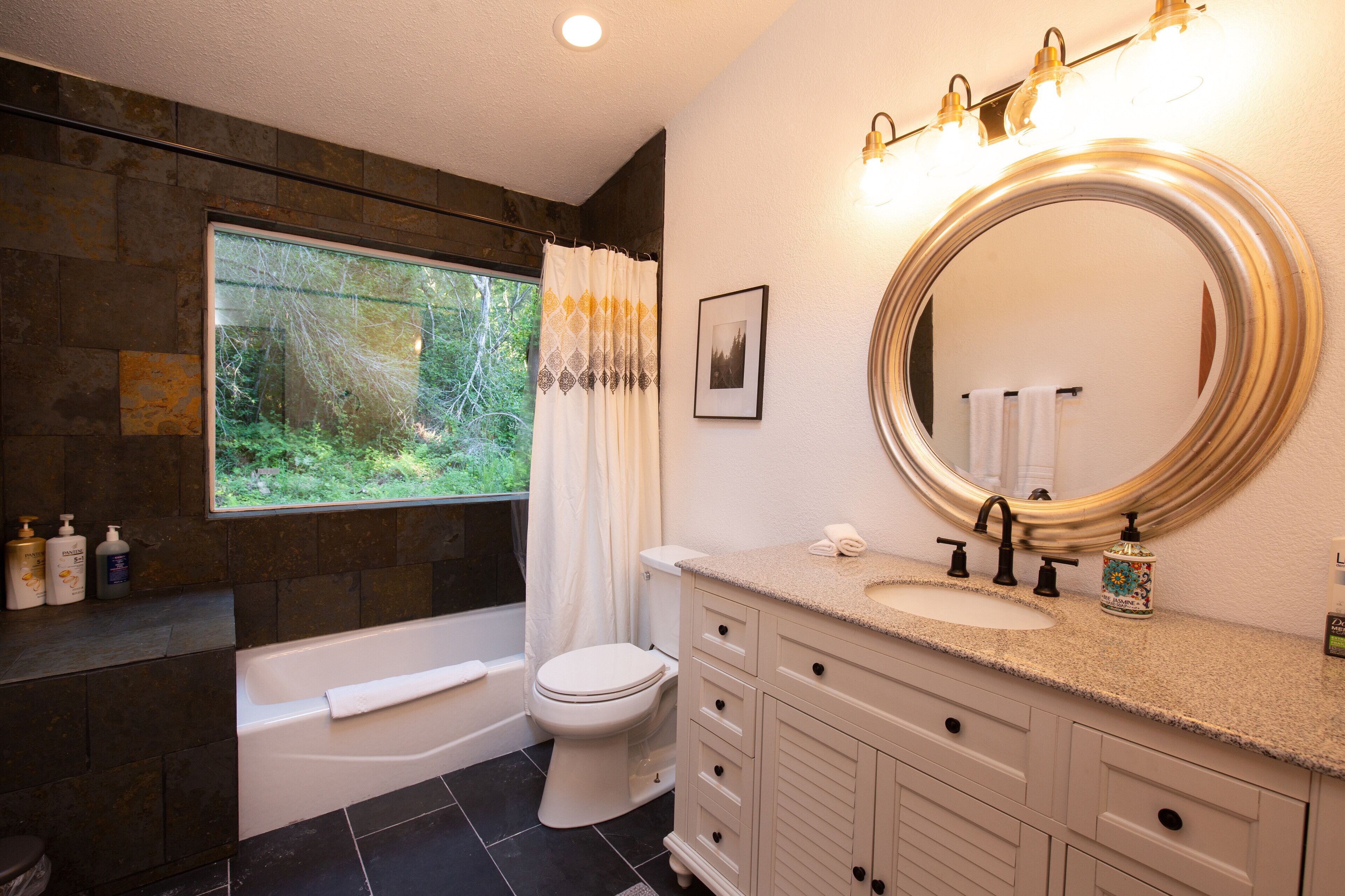 A bathroom with a bathtub, toilet, vanity with a sink, and a large mirror.