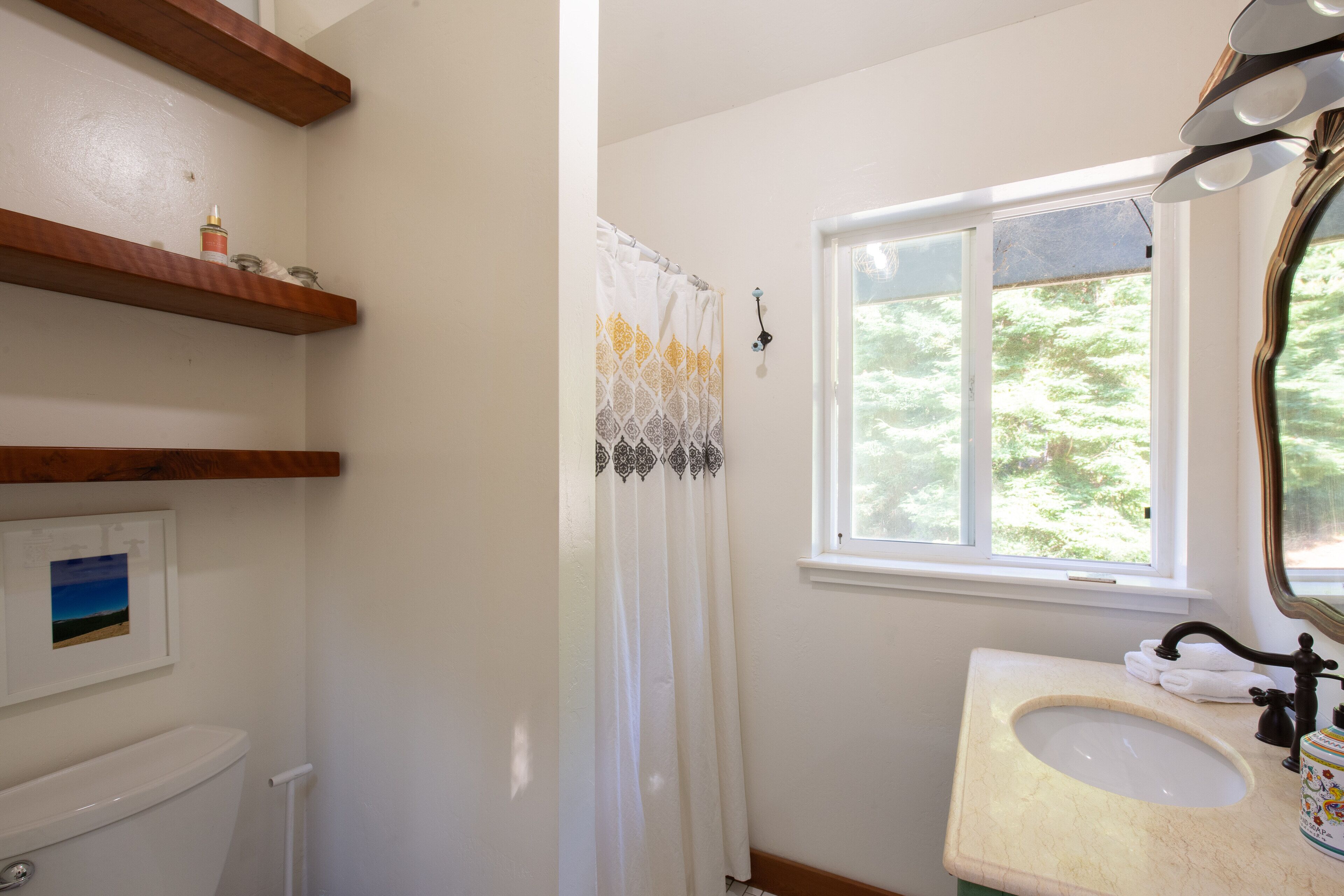 Un baño con inodoro, lavamanos, ventana y cortina de ducha.