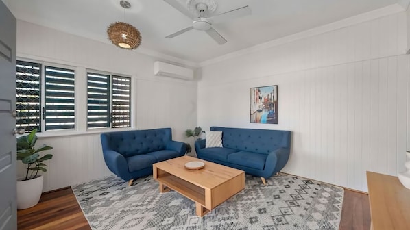 A living room with two blue sofas, a wooden coffee table, patterned rug, and a ceiling fan. - Convenient Location Cosy Home (Garbutt)