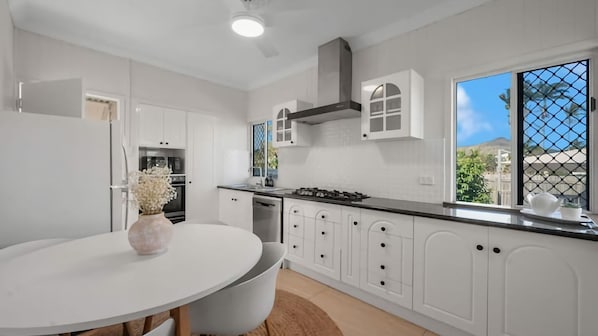 A modern kitchen with white cabinetry, a round dining table, and a view through a window.