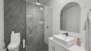 A modern bathroom with a glass-enclosed shower, a white toilet, a vanity with a sink, and a large mirror. - Convenient Location Cosy Home (Garbutt)