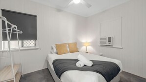 Et hotelværelse med seng, et vindue med gardin, en sengebordlampe og en aircondition.