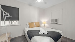 A hotel room with a bed, a window with a curtain, a bedside lamp, and an air conditioning unit. - Convenient Location Cosy Home (Garbutt)