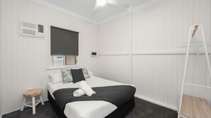 A bedroom with a bed, a small stool, a ladder, and a window with blinds.