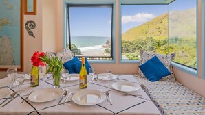 A dining area with a table set for two, large windows with a view of the beach, and a blue pendant light above the table.