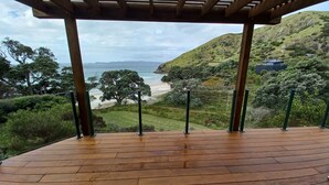 A wooden deck with a view of a coastal landscape, including hills and a beach.