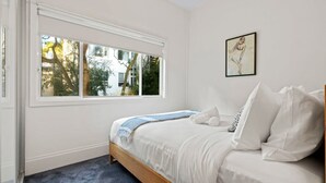 Une chambre avec une grande fenêtre, un lit recouvert de draps blancs et une œuvre d’art encadrée accrochée au mur.