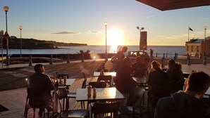 Un espace extérieur aménagé pour les repas, avec des tables et des chaises, offrant une vue sur un plan d’eau au coucher du soleil.