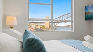 Una camera d'hotel con un letto, una finestra vista città, una lampada e un asciugamano sul letto.