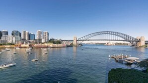 Panorama di una città con lungomare, un ponte importante, diverse imbarcazioni e grattacieli.