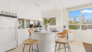 Una cucina moderna con mobili bianchi, un'isola centrale con sgabelli e vista sulla città attraverso ampie finestre.