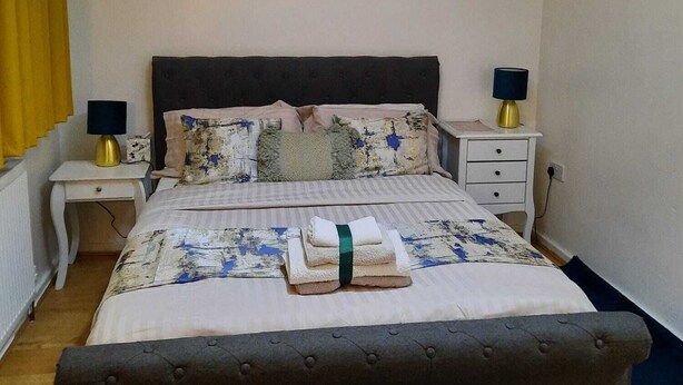 A bedroom with a bed, two bedside tables, a hanging lamp, a painting of a pier, and a window with curtains. - 2-bed House in the Heart of Woodhouse, Leeds (Leeds)