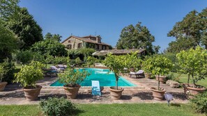 A pool area with lounge chairs, potted plants, and a stone building in the background.