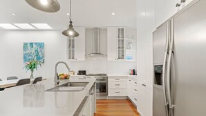 Une cuisine moderne avec des meubles blancs, un réfrigérateur en acier inoxydable et un îlot central doté d’un évier.